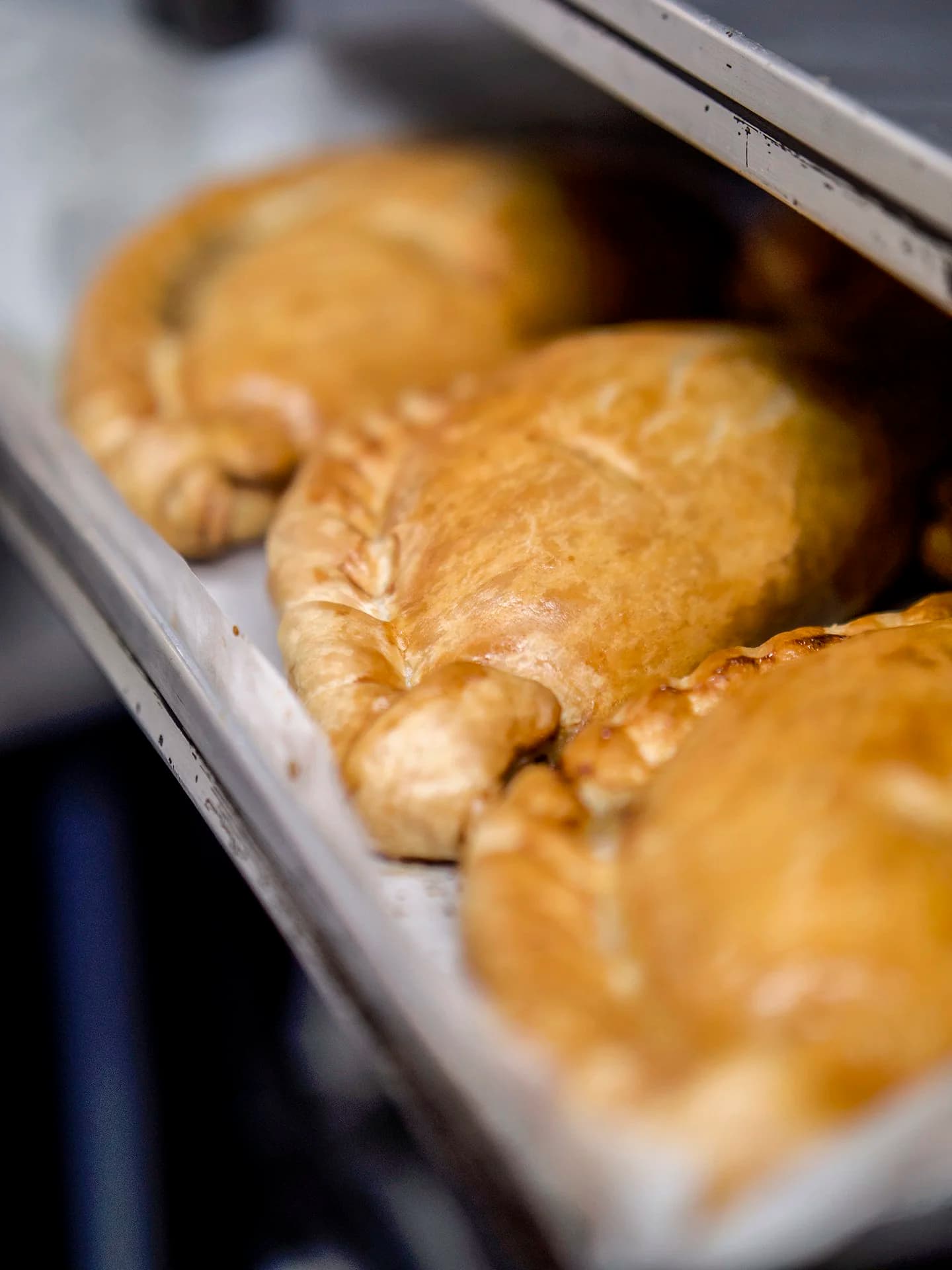 Hand-crimped pasties on a metal baking tray.